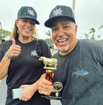 Two people wearing black shirts with logos, one holding a trophy, outdoors.