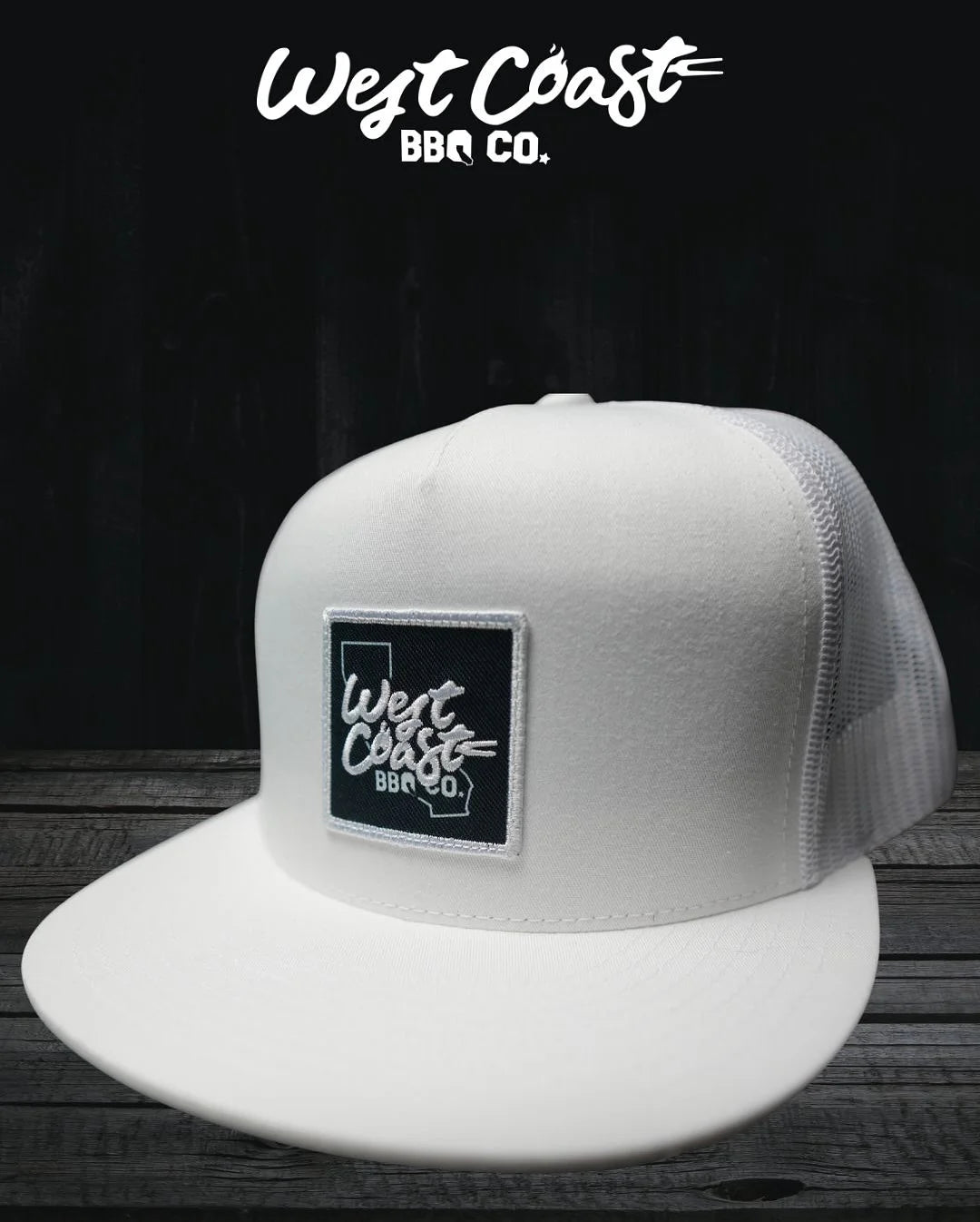 A white, flat-brimmed trucker hat with a white mesh back, featuring a square black patch with the "West Coast BBQ Co." logo.
