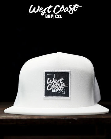 A white, flat-brimmed cap with a black square patch that has the "West Coast BBQ Co." logo embroidered in white.