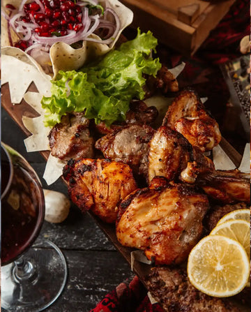 Plated dish of grilled chicken with garnishes on a wooden board, accompanied by a glass of red wine.