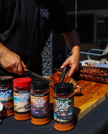 Person seasoning ribs with West Coast BBQ Co. products on a grill