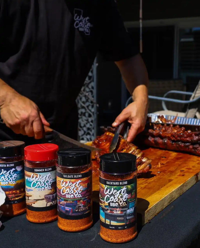 Person seasoning ribs with West Coast BBQ Co. products on a grill